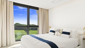 A modern bedroom with a large bed, a view of a green landscape, and a ceiling light.