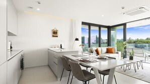 A modern kitchen with white cabinetry, a dining area with a white table and chairs, and a large window offering a view of greenery and a mountain.