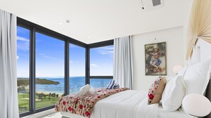 A bedroom with a large window overlooking a coastal landscape, a bed with white linens, and a painting on the wall. - B1101 Modern oceanview 2 bedroom condo (Cupecoy)