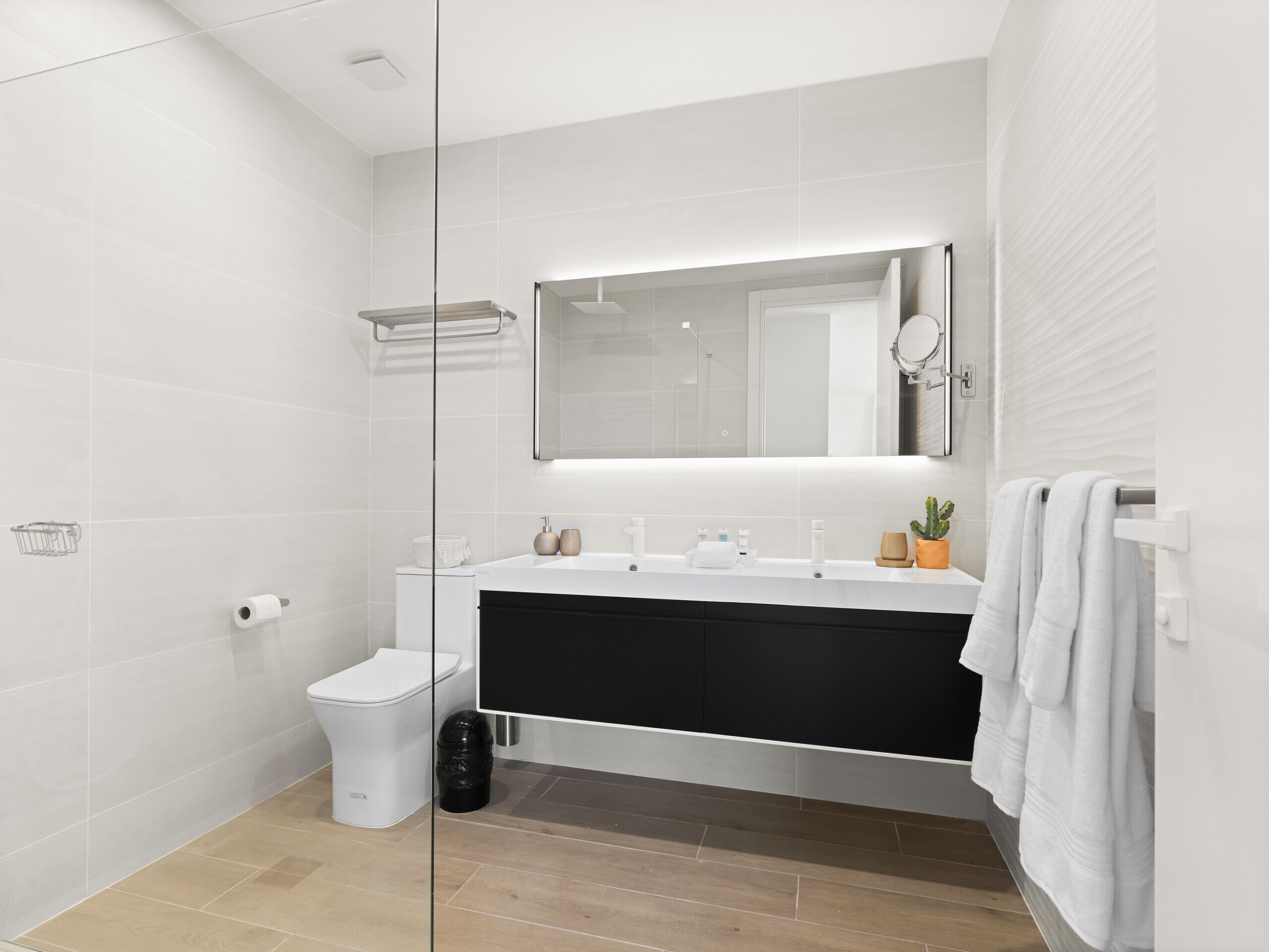 A modern bathroom with a white sink, black vanity, and a glass shower enclosure.