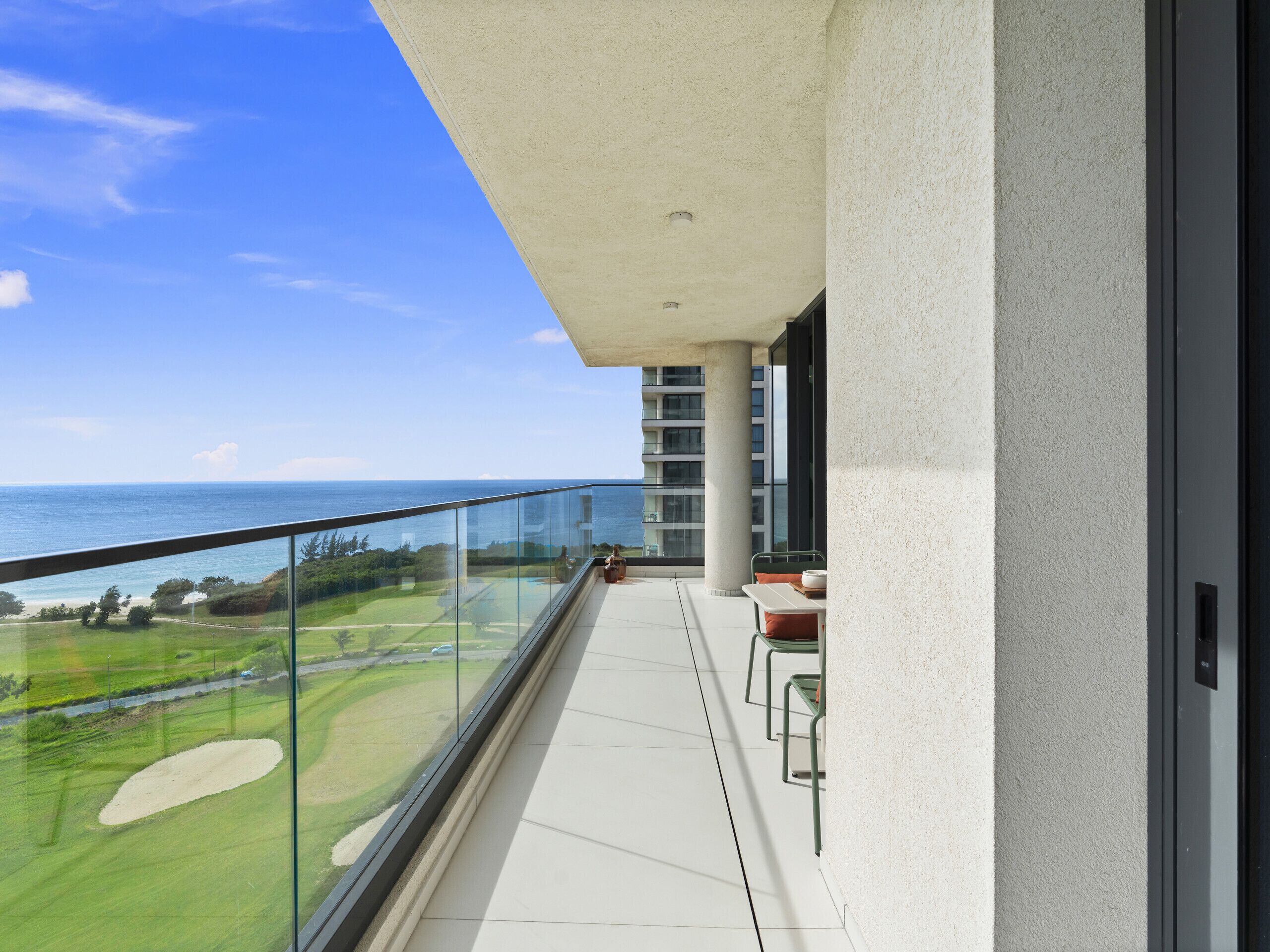 A balcony with a glass railing overlooking a golf course and the ocean.