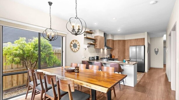 A modern kitchen with wooden cabinets, a central island, and a dining area with a large wooden table and chairs.