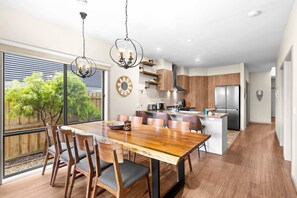 A modern kitchen with wooden cabinets, a central island, and a dining area with a large wooden table and chairs. - Seaside Retreat - Steps from Town and Beach (Ocean Grove)