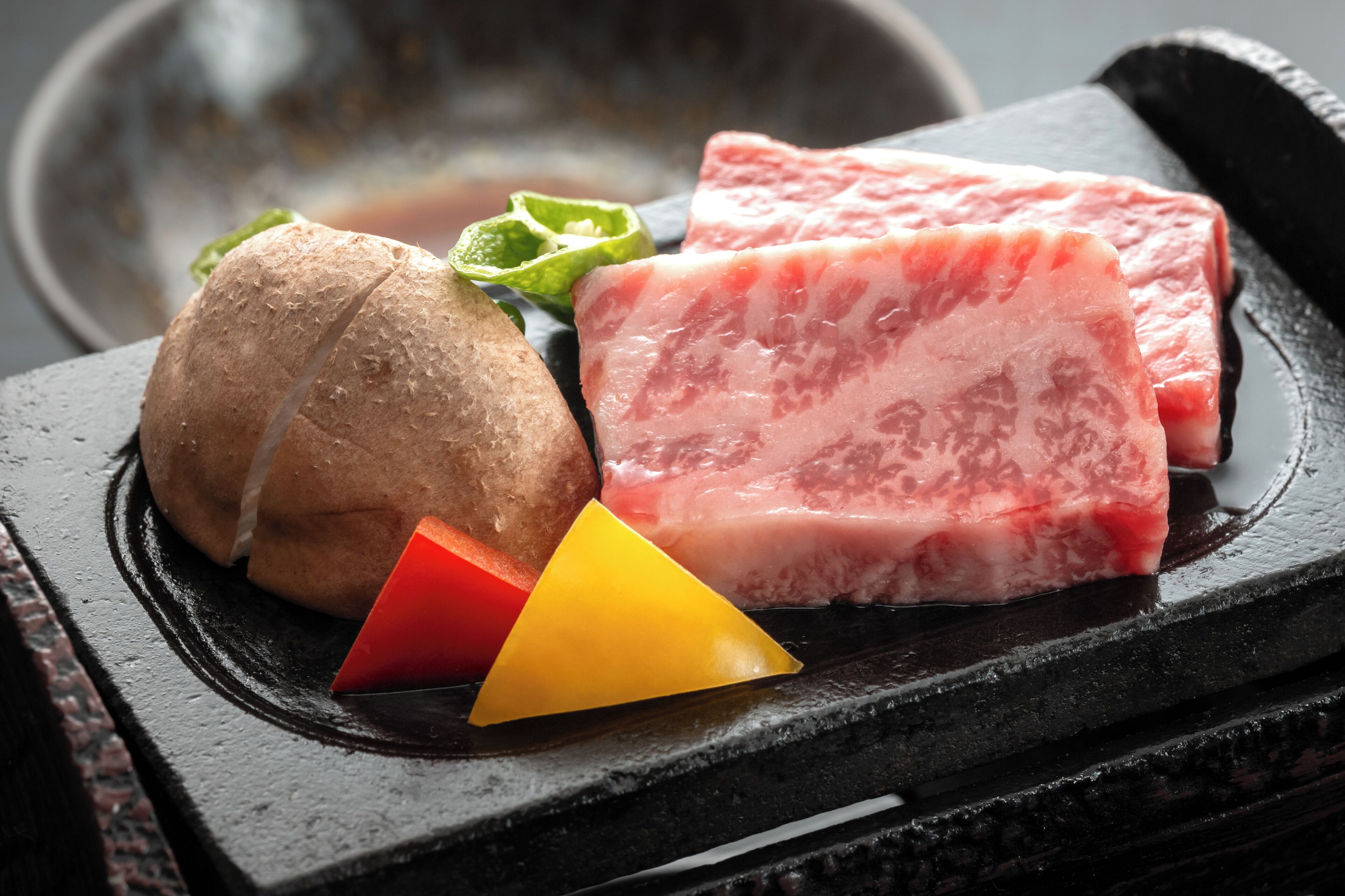 A black stone grill with raw meat, a whole potato, and a red and yellow triangular object.