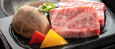 A black stone grill with raw meat, a whole potato, and a red and yellow triangular object.