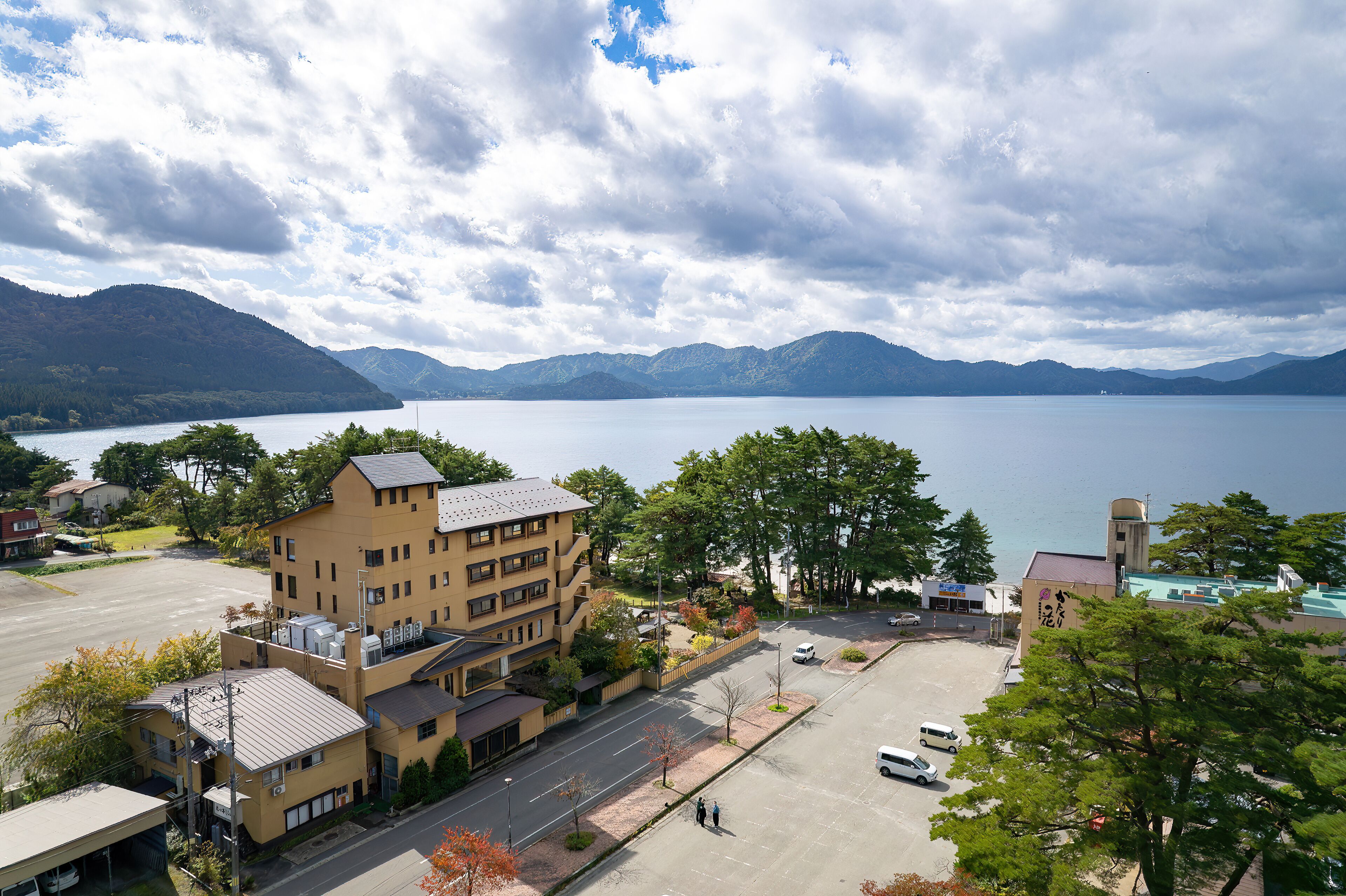 Un hotel de varios pisos con estacionamiento y vistas a un lago y montañas.