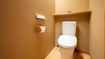 Een kleine badkamer met een toilet, een papieren handdoekdispenser en een plank boven het toilet.