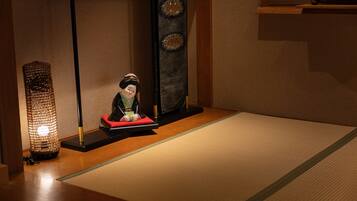 Une pièce de style japonais traditionnel, avec un sol recouvert de tatamis, un paravent en papier de riz (shoji) et une petite table sur laquelle est posée une poupée décorative.