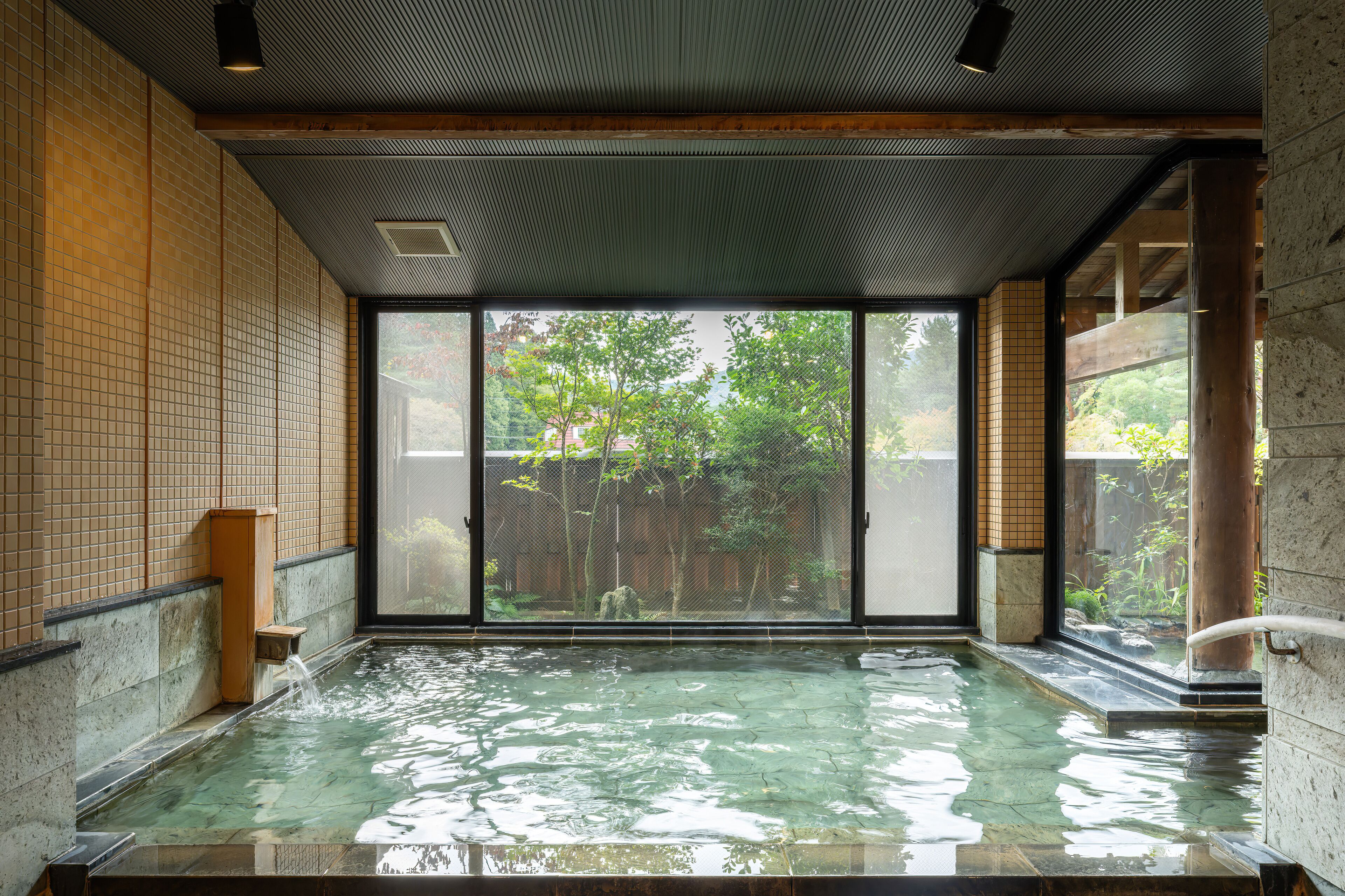Un onsen japonés tradicional con vistas despejadas del jardín circundante a través de amplios ventanales correderos.