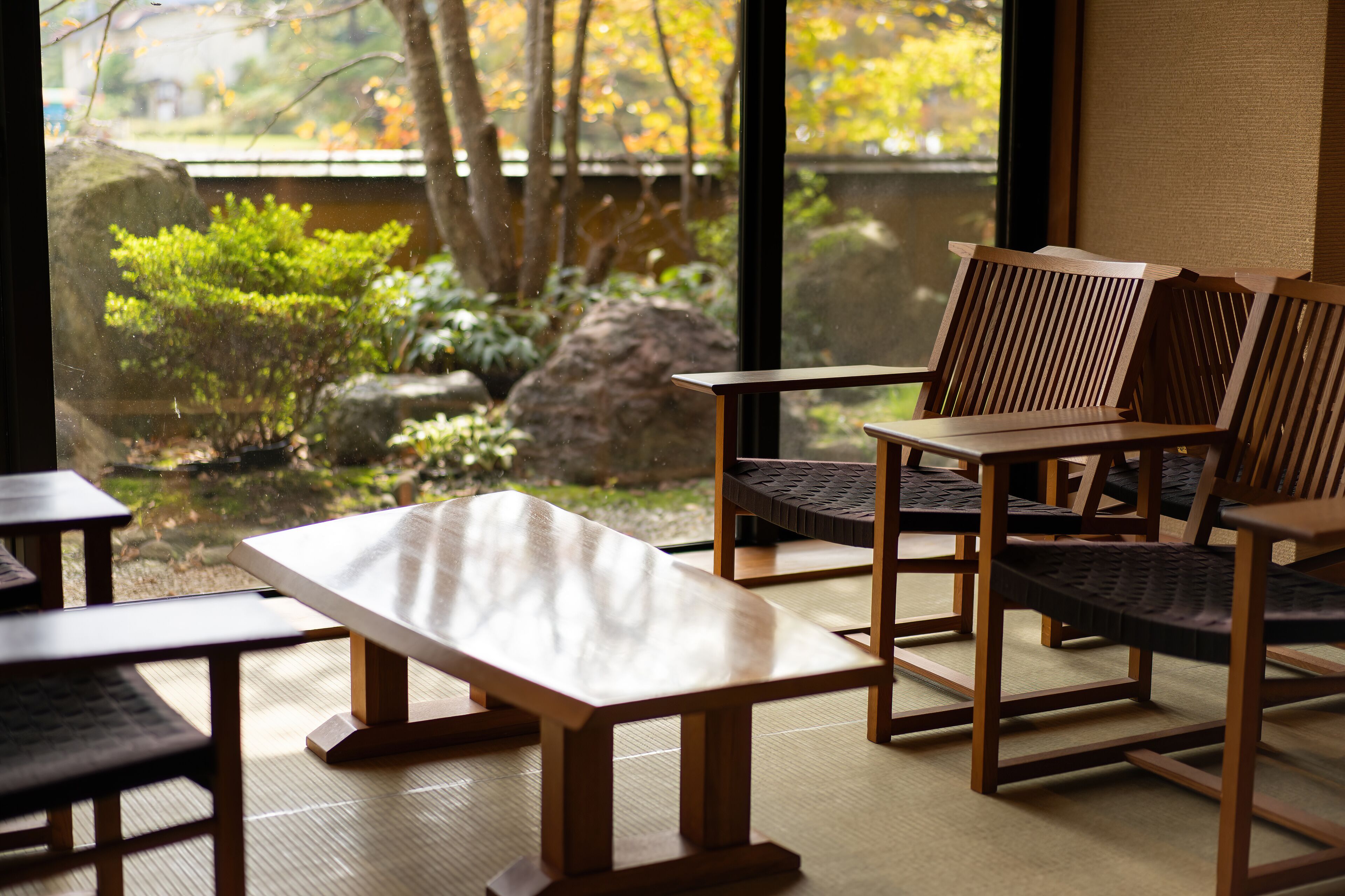 A traditional Japanese-style room with tatami flooring, wooden furniture, and a view of a garden through large windows.