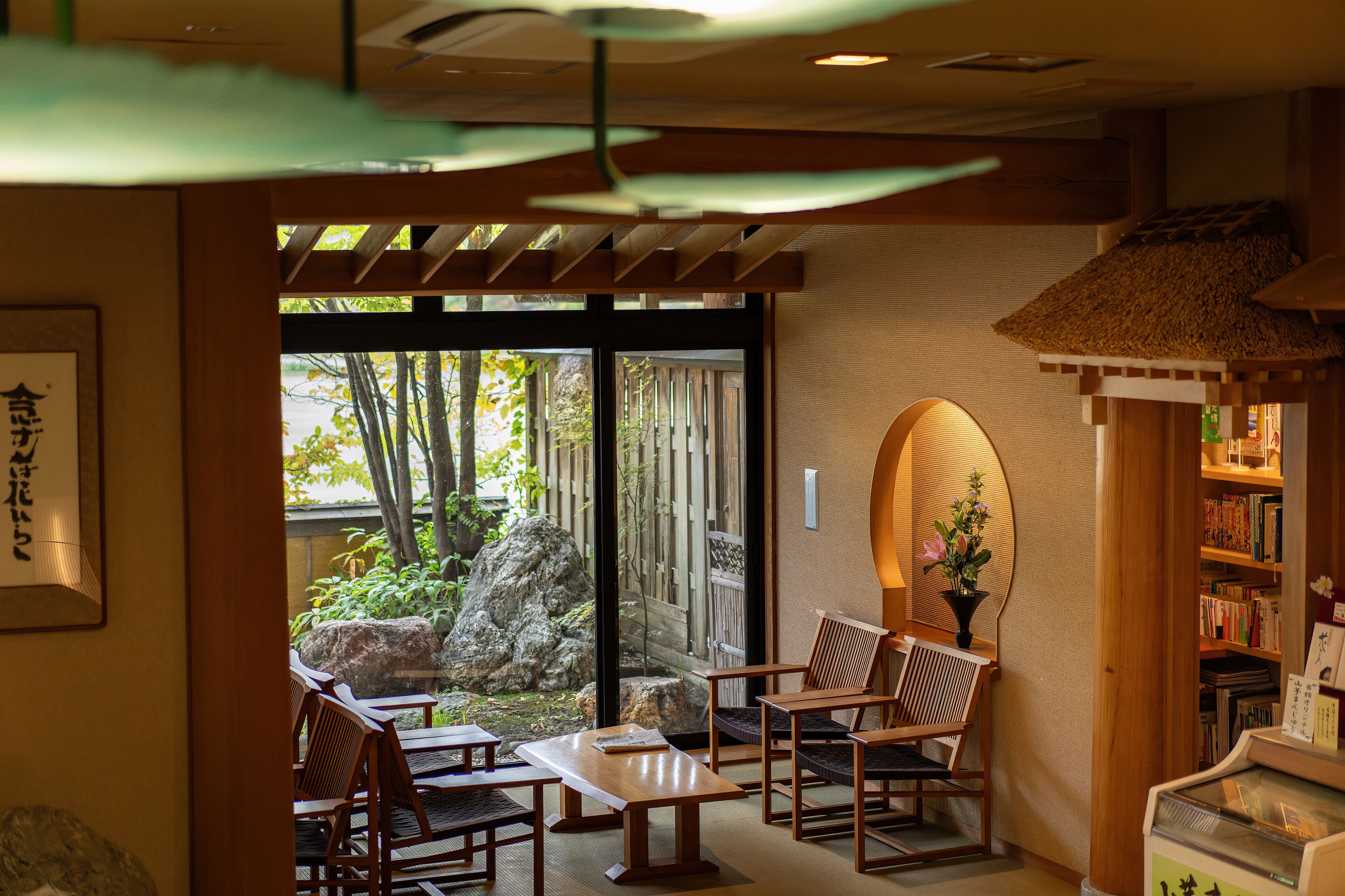 A traditional Japanese-style room with tatami flooring, wooden furniture, and a view of a garden through sliding doors.