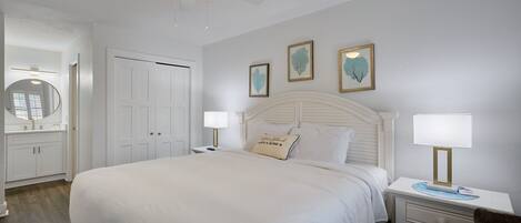 A neatly arranged bedroom with a large bed, bedside lamps, a ceiling fan, and framed artwork on the wall.