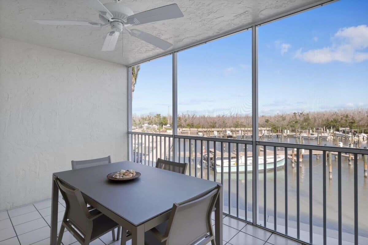 A balcony with a table and chairs, a ceiling fan, and a view of a marina.