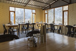 Enjoy meals in a cozy dining area with a wooden table, clear glassware, and a metal pitcher, surrounded by large windows offering a view of the surrounding trees.