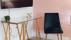 Una habitación moderna con una mesa de vidrio, una silla verde oscuro y un televisor montado.