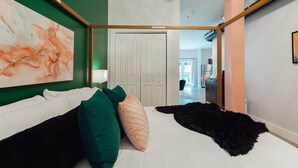 Un dormitorio con cama, almohadas verdes y blancas, un tapete mullido negro y un cuadro abstracto grande en la pared.