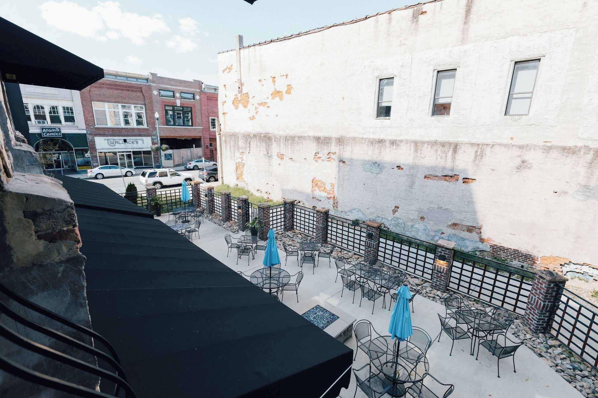 Un espace extérieur aménagé avec des tables et des chaises, un mur en briques et une vue sur la rue, avec des voitures garées et des bâtiments.