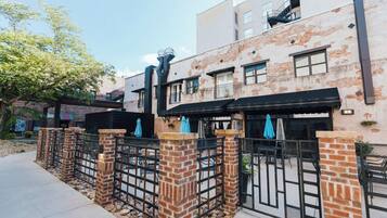 A row of brick buildings with outdoor seating areas, a gated entrance, and a clear sky.
