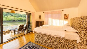 A bedroom with a large bed, a view of a river, and a balcony with chairs. - Feather Touch Hotels and Resorts Palolem (Canacona)