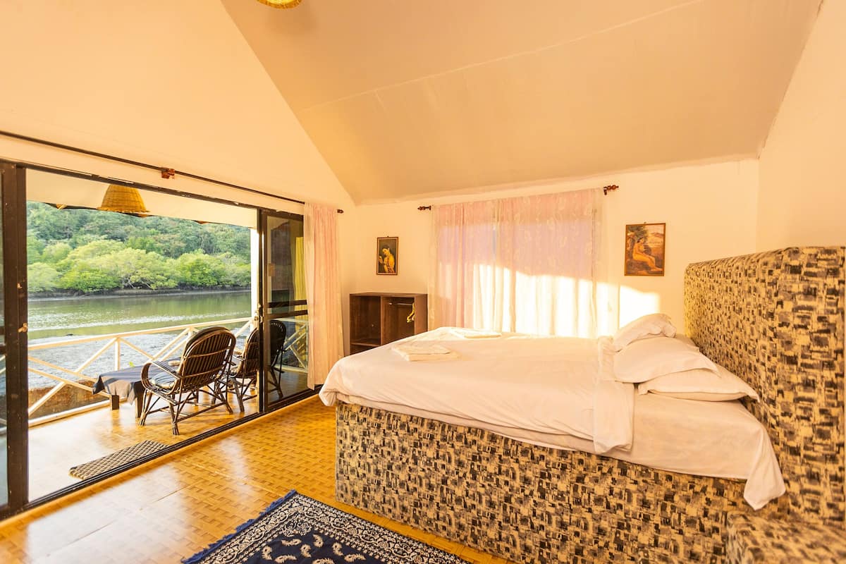 Quarto com uma cama grande, vista para um rio e varanda com cadeiras.