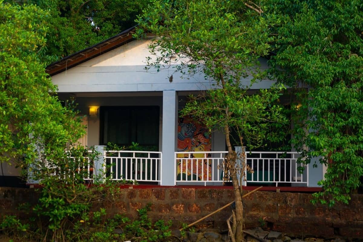 Uma casa com fachada branca, uma varanda com guarda-corpo branco e um mural colorido na parede.