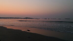 A beach at sunset with calm waves and boats in the distance. - Feather Touch Hotels and Resorts Palolem (Canacona)