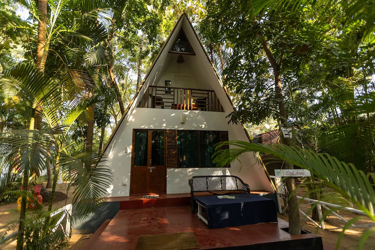 Um edifício em formato triangular com uma varanda, cercado por vegetação exuberante.