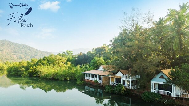 A serene lakeside property with multiple buildings, including a main house and a guest house, surrounded by lush greenery and a calm lake. - Feather Touch Hotels and Resorts Palolem (Canacona)