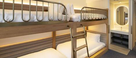 A bunk bed room with a wooden headboard, a ladder, and a small bathroom with a mirror and sink.