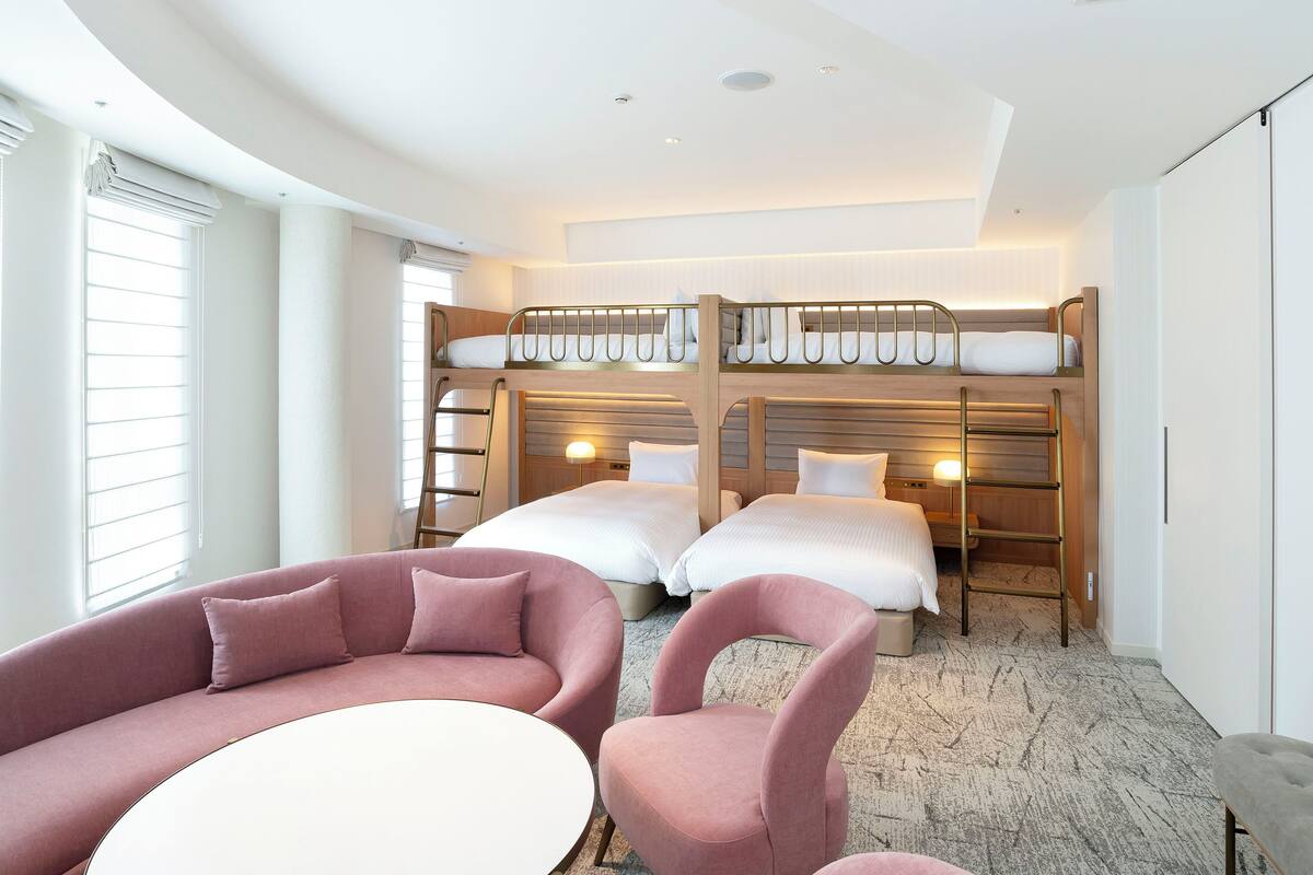 Una habitación de hotel con literas, un sofá, una silla y una mesita.