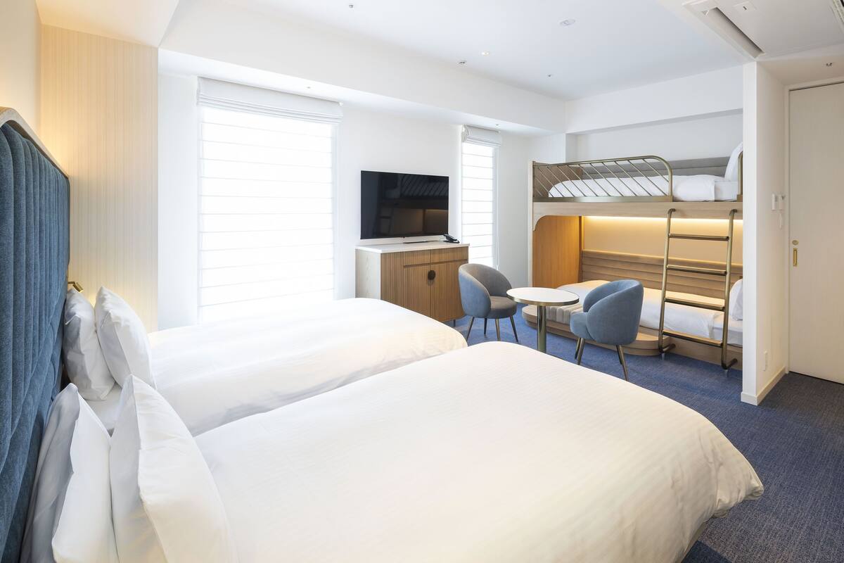 Una habitación de hotel con dos camas, un escritorio, un televisor y una litera.