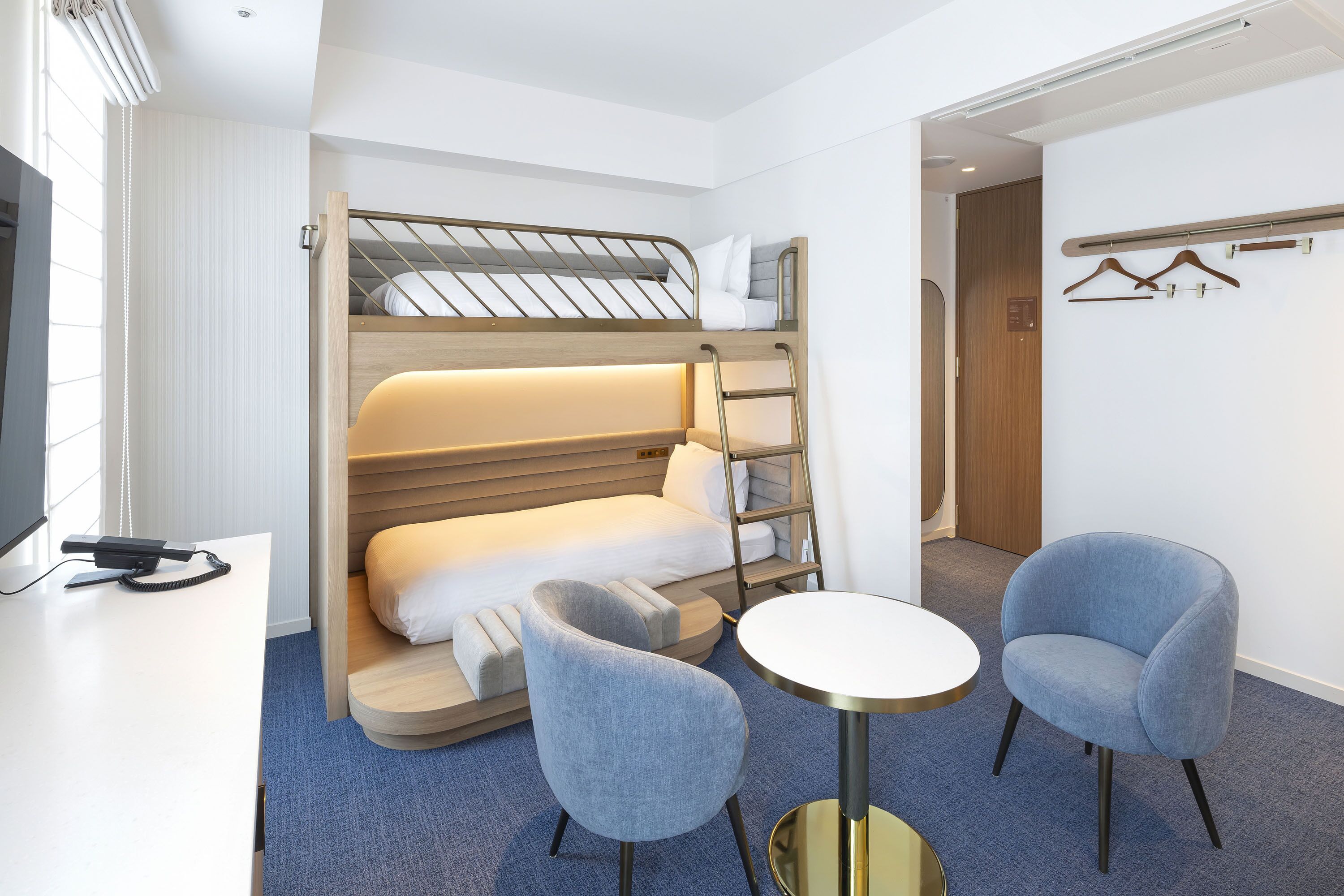 A hotel room with a bunk bed, a desk with a telephone, two armchairs, and a small round table.