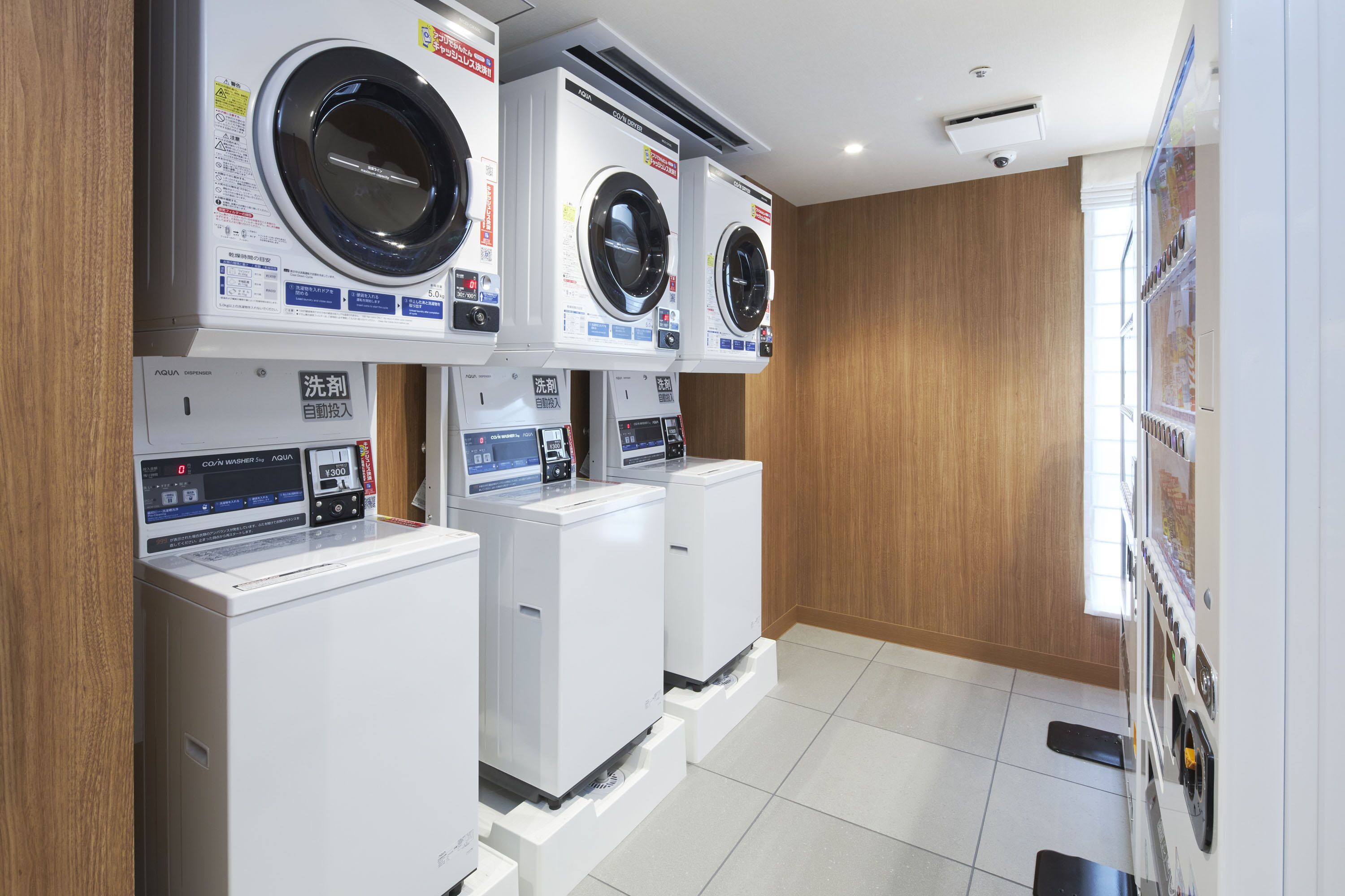 Une buanderie équipée de trois machines à laver et de trois sèche-linge superposés, avec des murs en bois et un sol carrelé.