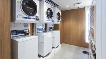 Une buanderie équipée de trois machines à laver et de trois sèche-linge superposés, avec des murs en bois et un sol carrelé.