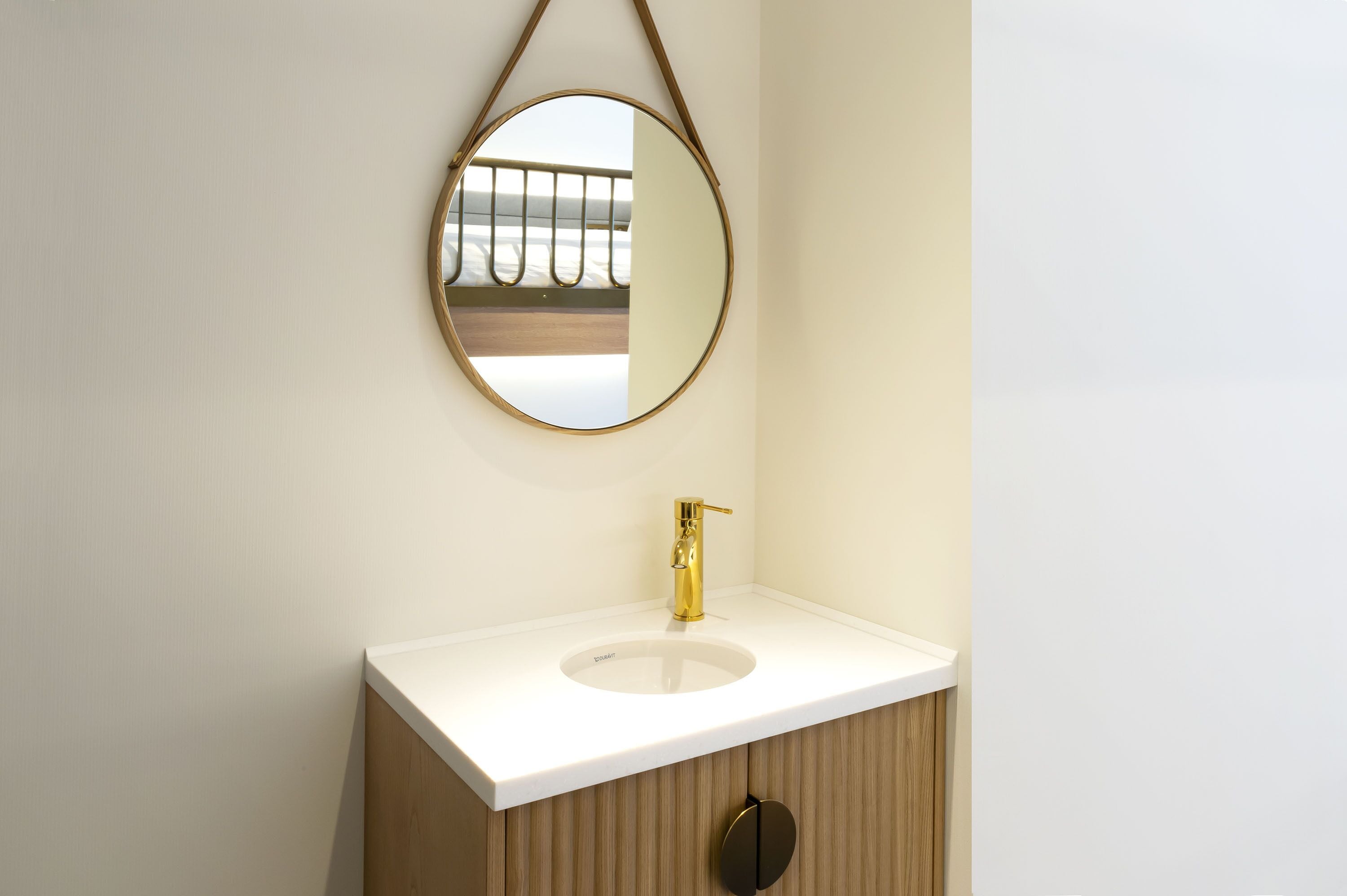 A bathroom with a white sink, gold faucet, and a round mirror.