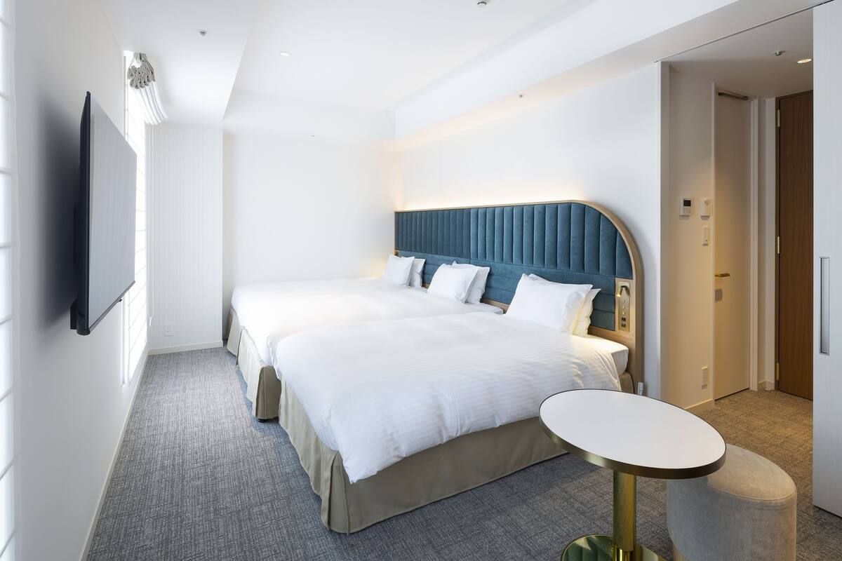 Habitación de hotel con una cama grande, una mesita de noche, un televisor de pantalla plana y una puerta que da a otra habitación.