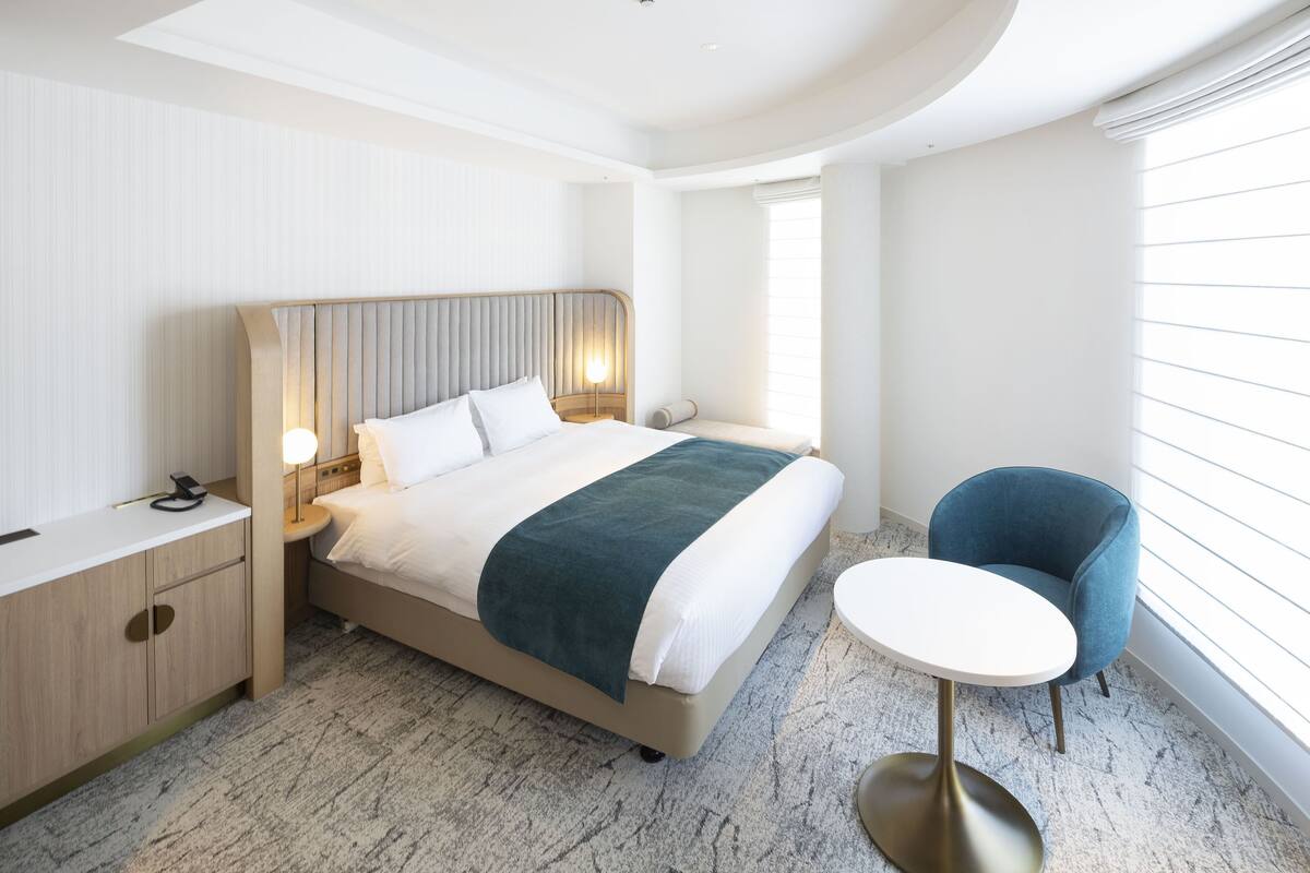 Una habitación de hotel moderna con una cama grande, mesita de noche, lámpara y una pequeña mesa redonda.