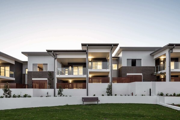 A modern multi-story residential building with balconies, a flat roof, and a well-maintained lawn.