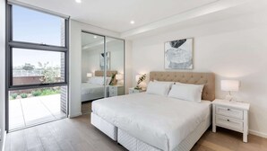 A modern bedroom with a large bed, a nightstand, a mirror, and a window. - Pristine 3-Bed Kiama Unit with Courtyard (Kiama)