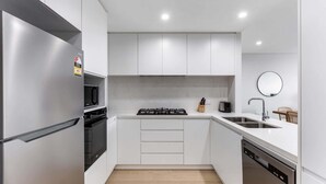 A modern kitchen with white cabinetry, a stainless steel refrigerator, a built-in oven, a gas stove, a microwave, a sink, and a dishwasher. - Pristine 3-Bed Kiama Unit with Courtyard (Kiama)