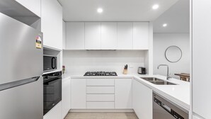A modern kitchen with white cabinetry, a built-in oven, a gas stove, a microwave, a sink, and a dishwasher. - 3-Bed Apartment in Beautiful Kiama with Study Nook (Kiama)