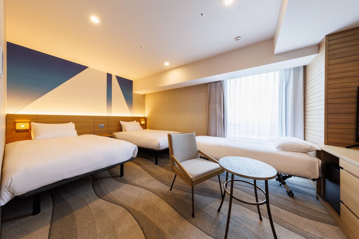 A hotel room with three beds, a small table, and a chair.