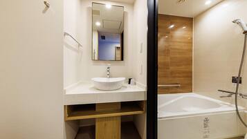 Un baño moderno con una bañera independiente, un lavabo con espejo y un mueble de tocador de madera.