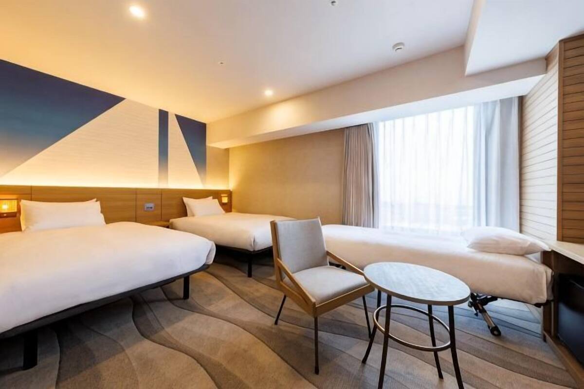 A hotel room with three beds, a small table, and a chair.