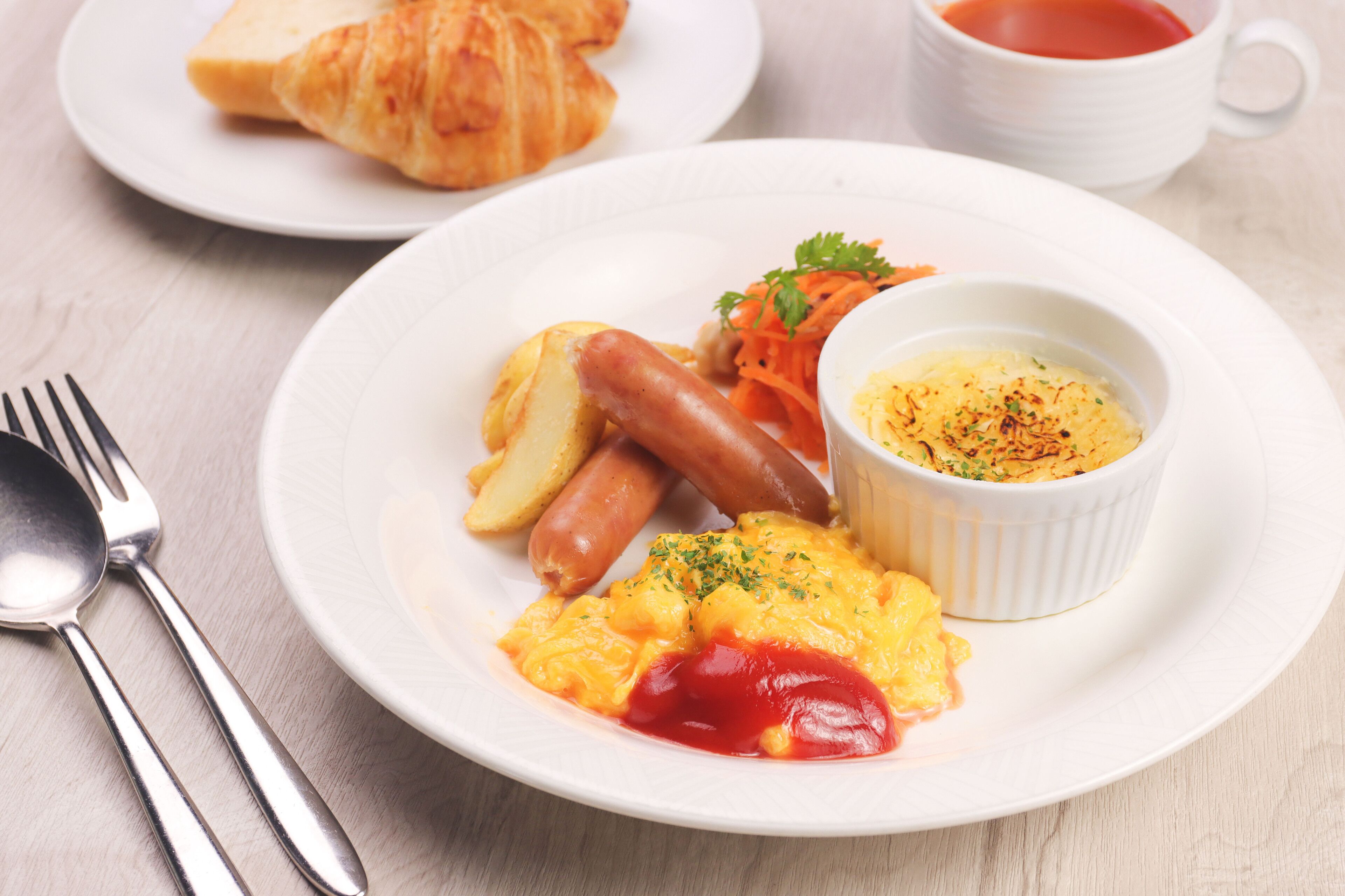 Un plato con alimentos para el desayuno, incluyendo salchichas, papas, huevos revueltos y un recipiente pequeño con salsa.