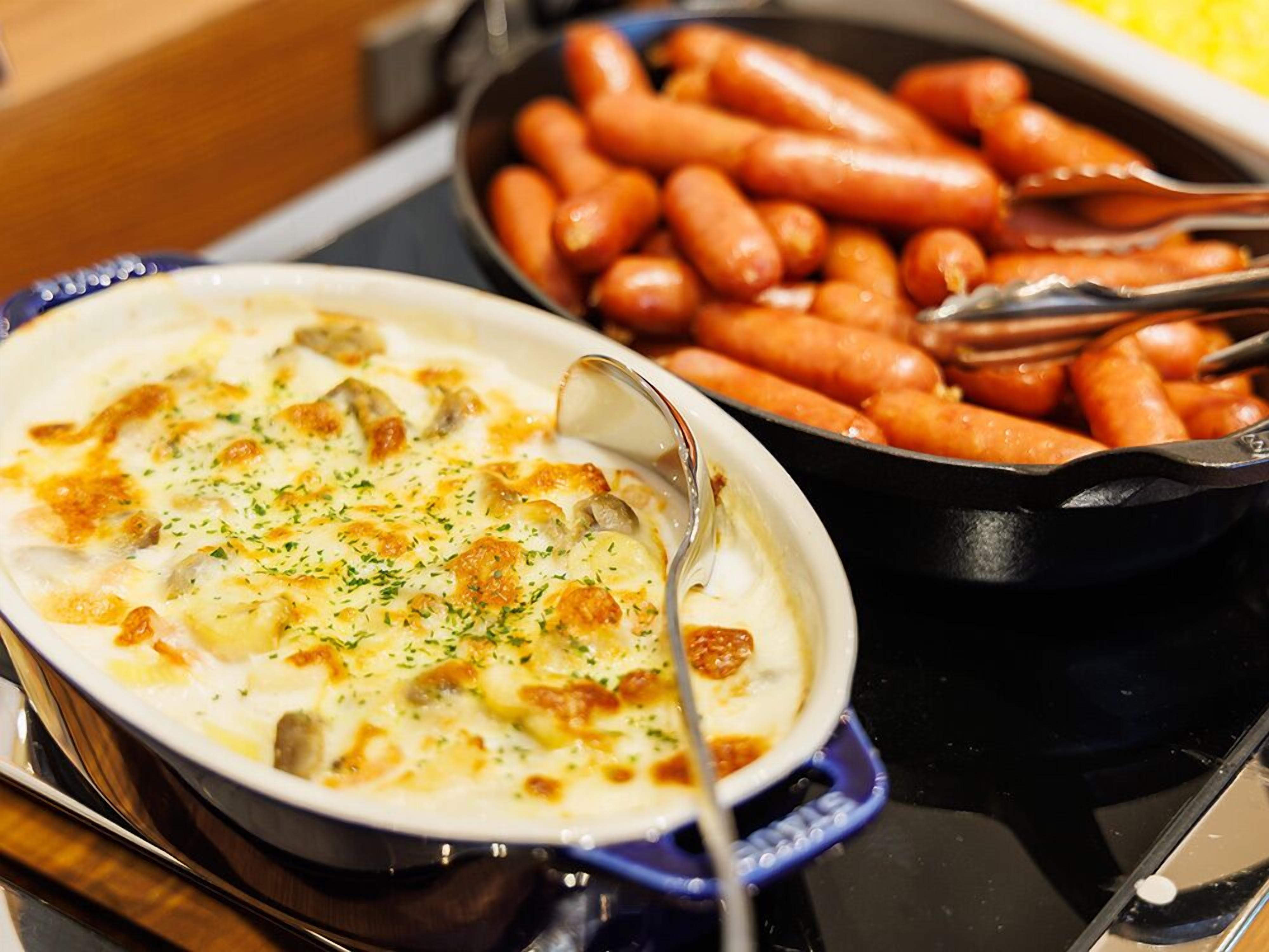 Eine Mahlzeit mit einem cremigen Gericht, bedeckt mit Käse und Kräutern, sowie eine Pfanne gegrillter Würstchen.