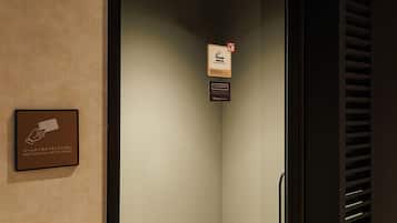 Een hotelkamer met een deur, een bord aan de muur met Japanse tekst, en een lijst met een bordje met Engelse tekst dat aangeeft de kamerkaart op de sensor te houden.