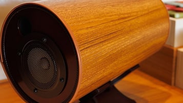 A wooden speaker with a circular design, mounted on a stand.