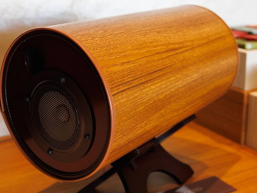 A wooden speaker with a circular design, mounted on a stand.