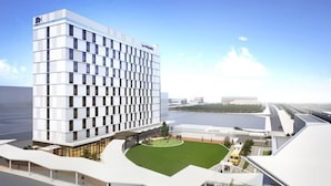 Un hotel moderno con un patio central, un edificio grande con una fachada de ventanas enrejada y vistas al agua.